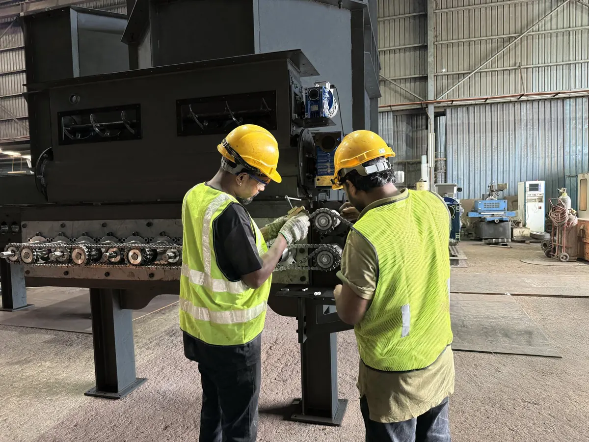 Two engineers in hard hats and hi-vis vests adjusting the chain drive on a pyrolysis unit in the workshop